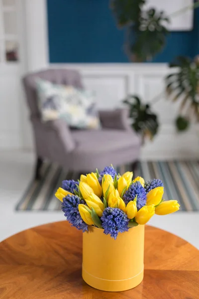 Bunch of blue hyacinths and yellow tulips on white table. Present for a girl. Flowers bouquet in box. Sunny spring morning.