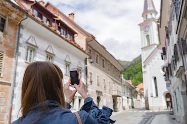 Genç turist kız street tarafından küçük bir kasaba olan Slovenya, Europe dağlar yürür. Eski püskü eski evleri cephe ve çatı. Katolik Kilisesi ve şehir merkezi
