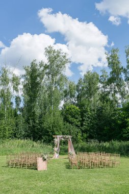 Gelin, damat ve misafirleri bekleyen açık hava düğün için güzel bir ortam. Çiçeklerle süslenmiş ahşap sandalyeler, bir ormanda düğün töreninin yapıldığı bölgedeler.