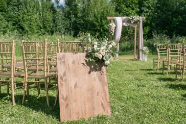 Gelin, damat ve misafirleri bekleyen açık hava düğün için güzel bir ortam. Çiçeklerle süslenmiş ahşap sandalyeler, bir ormanda düğün töreninin yapıldığı bölgedeler.
