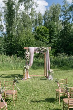 Gelin, damat ve misafirleri bekleyen açık hava düğün için güzel bir ortam. Çiçeklerle süslenmiş ahşap sandalyeler, bir ormanda düğün töreninin yapıldığı bölgedeler.