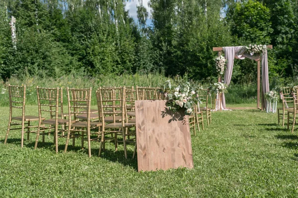 Gelin, damat ve misafirleri bekleyen açık hava düğün için güzel bir ortam. Çiçeklerle süslenmiş ahşap sandalyeler, bir ormanda düğün töreninin yapıldığı bölgedeler. — Stok fotoğraf