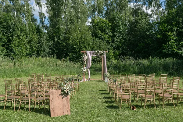 Gelin, damat ve misafirleri bekleyen açık hava düğün için güzel bir ortam. Çiçeklerle süslenmiş ahşap sandalyeler, bir ormanda düğün töreninin yapıldığı bölgedeler. — Stok fotoğraf