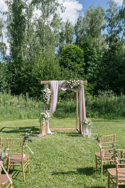 Gelin, damat ve misafirleri bekleyen açık hava düğün için güzel bir ortam. Çiçeklerle süslenmiş ahşap sandalyeler, bir ormanda düğün töreninin yapıldığı bölgedeler.