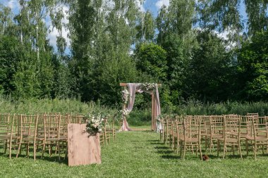 Gelin, damat ve misafirleri bekleyen açık hava düğün için güzel bir ortam. Çiçeklerle süslenmiş ahşap sandalyeler, bir ormanda düğün töreninin yapıldığı bölgedeler.