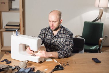 bir iğne ve iplik el ile. Bir terzi çalışan ve bir dikiş makinesi bir tekstil Studio'yu kullanarak iyi görünümlü genç adam.