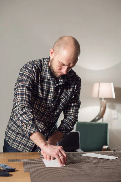 Styckning ulltyg. linjemönster. Flugor av ylle tyg. Ung man arbeta som skräddare och använda en symaskin i en Textilkammare. — Stockfoto