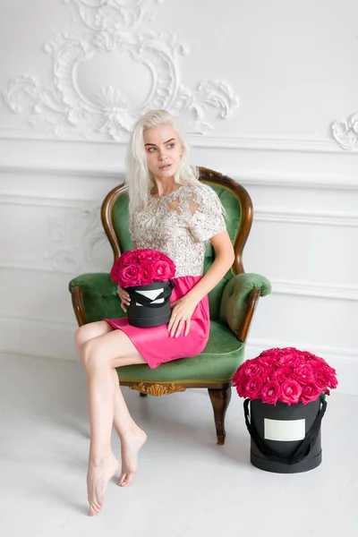 Menina bonita nova com rosto bonito e cabelo loiro longo. Mulher senta-se e segurando caixa preta com rosas rosa. Interior de luxo — Fotografia de Stock