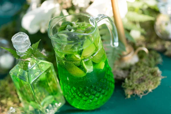 Forest decor. Lemonade pitcher with lime, mint and ice on table — Stock Photo, Image