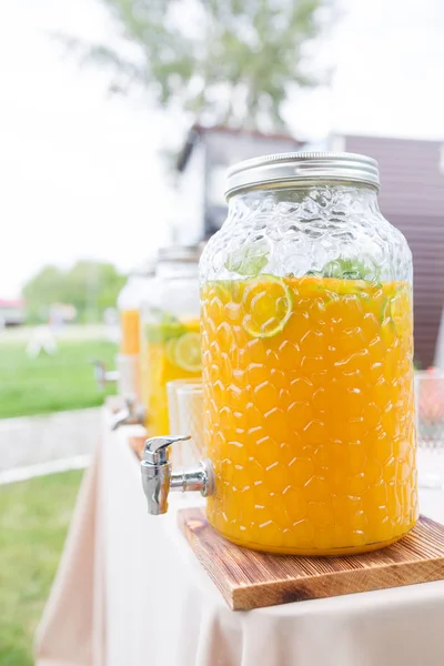 Glass bank of lemonade with sliced citrus fruits on a buffet table. Summer party outdoor. Detox. — Stock Photo, Image