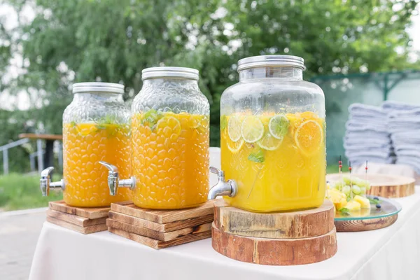 Glass bank of lemonade with sliced citrus fruits on a buffet table. Summer party outdoor. Detox. — Stock Photo, Image