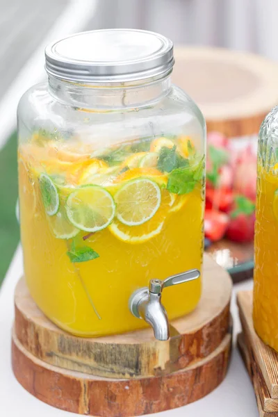 Skleněná banka limonády s plátky citrusových plodů na bufetového stolu. Venkovní letní party. Detoxikační. — Stock fotografie