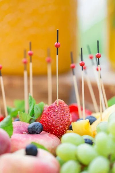 Wooden plate with sliced fruits and berries on a buffet table. Summer party outdoor. Vertical photo — Stock Photo, Image