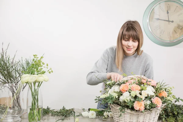 Florista feminina sorridente. Oficina floral - mulher fazendo uma bela composição de flores um buquê em uma cesta de vime. Conceito de floricultura — Fotografia de Stock
