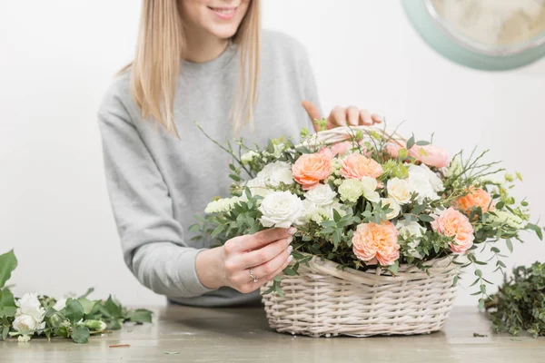 Una florista sonriente. El taller floral - la mujer que hace la composición hermosa de flores el ramo en la cesta de mimbre. Concepto floristería — Foto de Stock