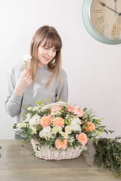 Una florista sonriente. El taller floral - la mujer que hace la composición hermosa de flores el ramo en la cesta de mimbre. Concepto floristería — Foto de Stock