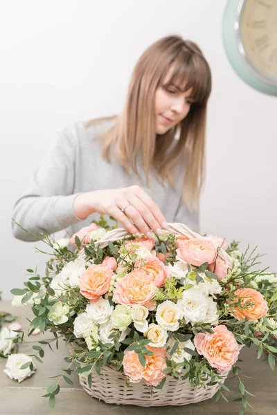 Una florista sonriente. El taller floral - la mujer que hace la composición hermosa de flores el ramo en la cesta de mimbre. Concepto floristería — Foto de Stock