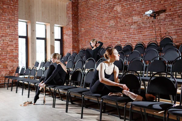 芭蕾的概念。年轻的芭蕾舞女演员坐在大厅的黑色椅子上。黑人紧身衣裤的彩排中的妇女。准备戏剧表演 — 图库照片
