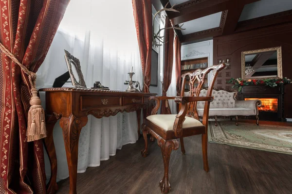 Old studying room with fabric armchairs and wooden table. Classic bookcase filled with books. Fireplace