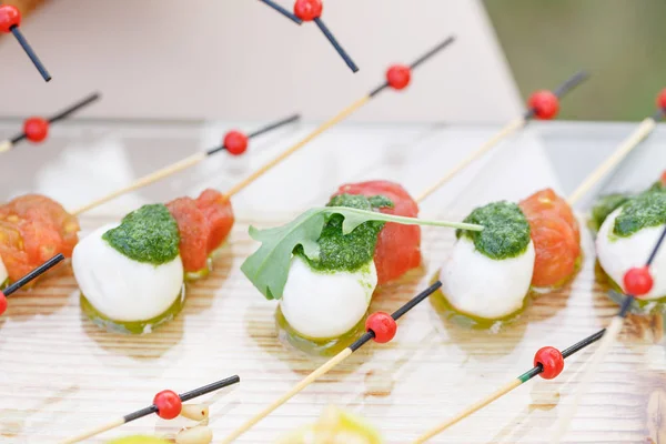 Förrätt, Caprese. Körsbärstomater, mozzarella och basilika på spett. . Pestosås. Välsmakande buffé bord. Sommarfest utomhus. — Stockfoto