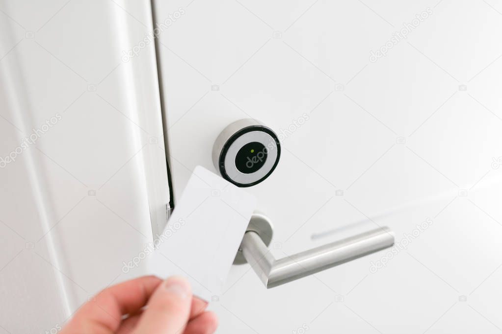 Hotel door - Young man holding a keycard in front of the electronic sensor of a room door. Concept travel or business trip