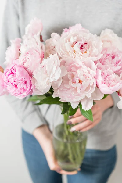 Flores de peônia bonito e adorável em mãos de mulheres.. muitas pétalas em camadas. Bunch rosa pálido peônias flores luz fundo cinza. Papel de parede, foto vertical — Fotografia de Stock