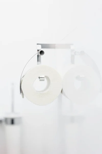 Bílé role měkkých toaletního papíru úhledně visí na moderní chrom držák na zdi koupelny lehké zrcadlo. — Stock fotografie