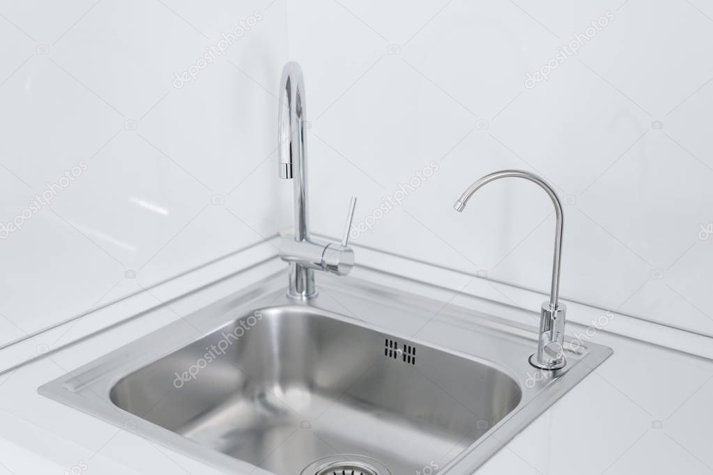 Metal chrome sink with two taps, plain and filtered water. Fragment of modern kitchen with counter and sink. Detail of interior apartment.