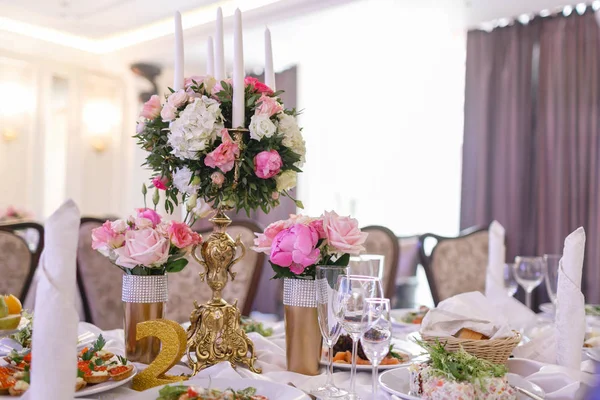 Fehér gyertyák fém arany csilláron állnak asztalokon a luxus esküvői recepción az étteremben. stílusos dekoráció és díszítés — Stock Fotó