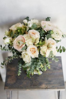 Beyaz güller sevdiceğim ahşap bir masa üzerinde bir buket düğün. Bir sürü yeşillik, asimetrik modern gelin grup darmadağınık.