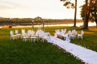 günbatımı Nehri üzerinde. Romantik düğün töreni. Şerit ve çiçeklerle bir yeşil çim üzerinde beyaz ahşap sandalyeler. Konuklar güzel Ofis koltukları