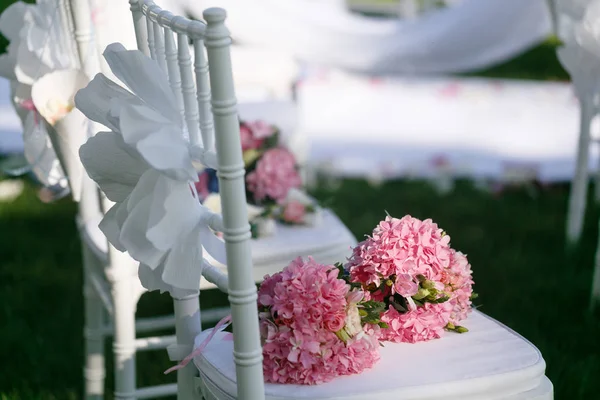 Tapes fly in the wind. Romantic wedding ceremony. White wooden chairs with ribbon and flowers on a green lawn. Nice armchairs for guests — Stock Photo, Image