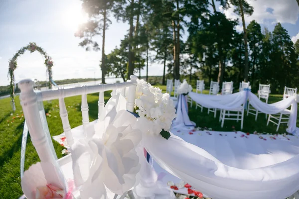 I nastri volano nel vento. Cerimonia di matrimonio romantica. Sedie bianche in legno con nastro e fiori su un prato verde. Belle poltrone per gli ospiti — Foto Stock