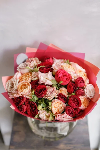 Luminoso bouquet rosso di bellissimi fiori sul tavolo di legno. Concetto di fioritura. Colori primaverili. il lavoro del fioraio in un negozio di fiori. Foto verticale — Foto Stock