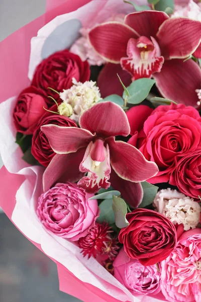 Leuchtend roter Strauß schöner Blumen auf dem Holztisch. Floristikkonzept. Frühlingsfarben. die Arbeit des Blumenhändlers in einem Blumenladen. vertikales Foto — Stockfoto