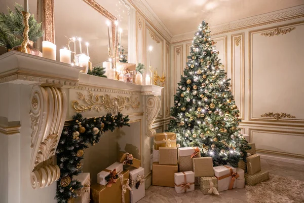 Christmas evening in the light of candles and garlands. Classic luxurious apartments with decorated christmas tree and presents. Living with fireplace, columns and stucco.