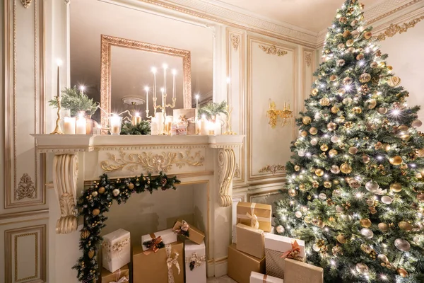 Christmas evening in the light of candles and garlands. Classic luxurious apartments with decorated christmas tree and presents. Living with fireplace, columns and stucco.