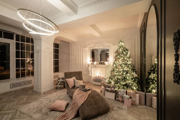 Julafton i ljuset av ljus och girlanger. Klassiska lyxiga lägenheter med dekorerad julgran och presenter. Leva med öppen spis, kolonner och stuckatur. — Stockfoto