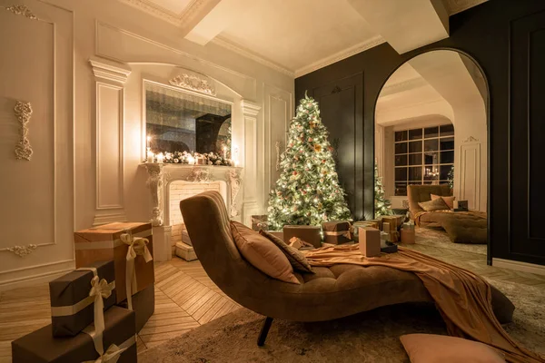 Noche de Navidad a la luz de velas y guirnaldas. Apartamentos de lujo clásicos con árbol de Navidad decorado y regalos. Vivir con chimenea, columnas y estuco . — Foto de Stock