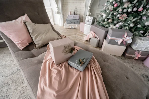 Regalos de Navidad en el sofá, árbol con adornos en el fondo. Bolas de Navidad, lazo de cinta, copos de nieve, piñas y luces . — Foto de Stock