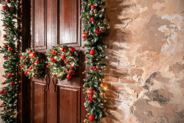 Házi bejárat díszített ünnepekre. Karácsonyi dekoráció. Két koszorú és fenyőágak koszorúja. Nagy faajtó — Stock Fotó