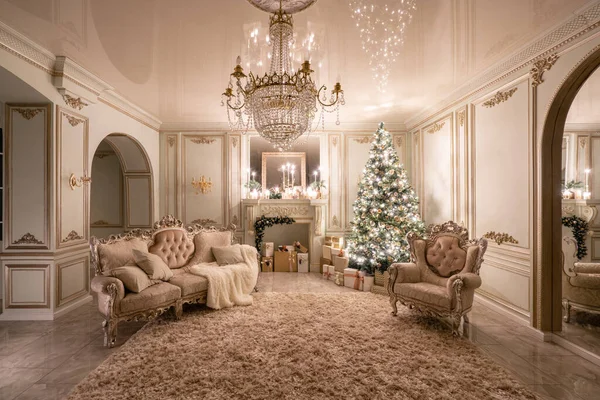 Christmas evening in the light of candles and garlands. Classic luxurious apartments with decorated christmas tree and presents. Living with fireplace, columns and stucco.