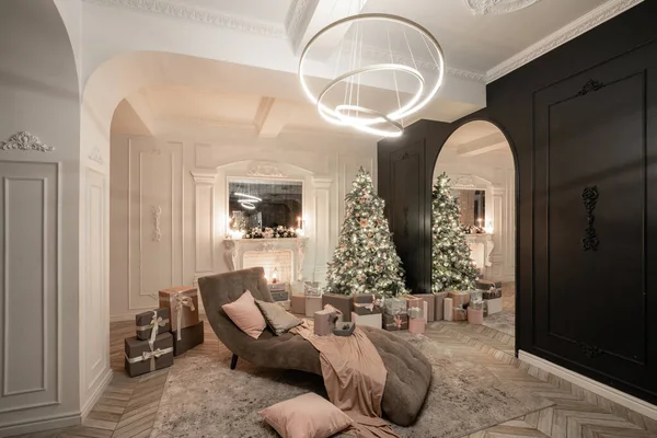 Christmas evening in the light of candles and garlands. Classic luxurious apartments with decorated christmas tree and presents. Living with fireplace, columns and stucco.