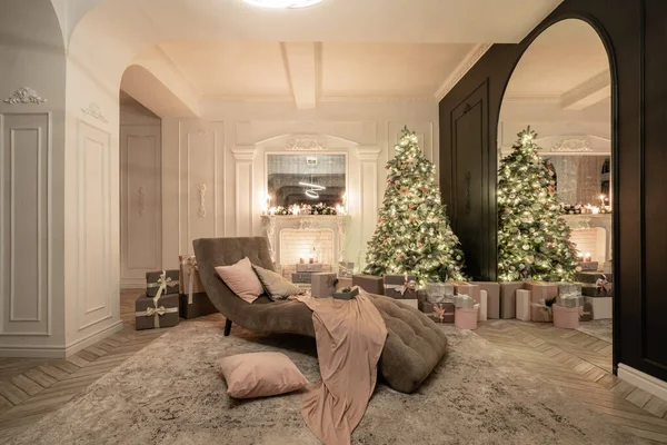 Christmas evening in the light of candles and garlands. Classic luxurious apartments with decorated christmas tree and presents. Living with fireplace, columns and stucco.