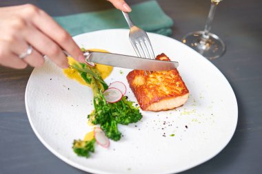 Restoranda öğle yemeği, bir kadın somon bifteği filetosunu keser ve genç brokoli ile süslenir. Restoran menüsü, bir dizi farklı yemeğin fotoğrafları.