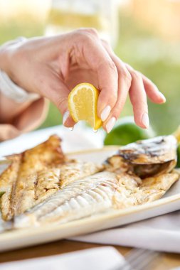 Restoranda öğle yemeği, kızarmış dorado balığı ve kızarmış kuşkonmaz yiyen bir kadın. Tabak bir dilim limonla süslenmiş. Restoran menüsü
