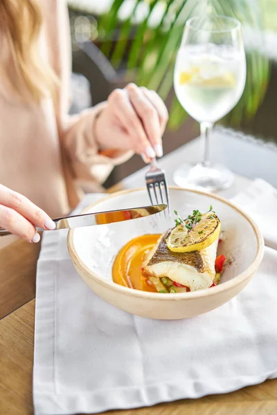 Roasted Halibut with vegetables, paprika pepper and pumpkin cream. Lunch in a restaurant, a woman eats delicious and healthy food. Dish decorated with a slice of lemon. Restaurant menu — Stock Photo, Image