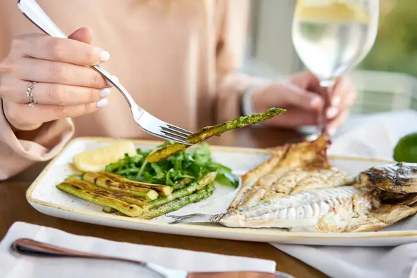 Lunch in a restaurant, a woman eats roasted dorado fish with grilled asparagus. Dish decorated with a slice of lemon. Restaurant menu — Stock Photo, Image