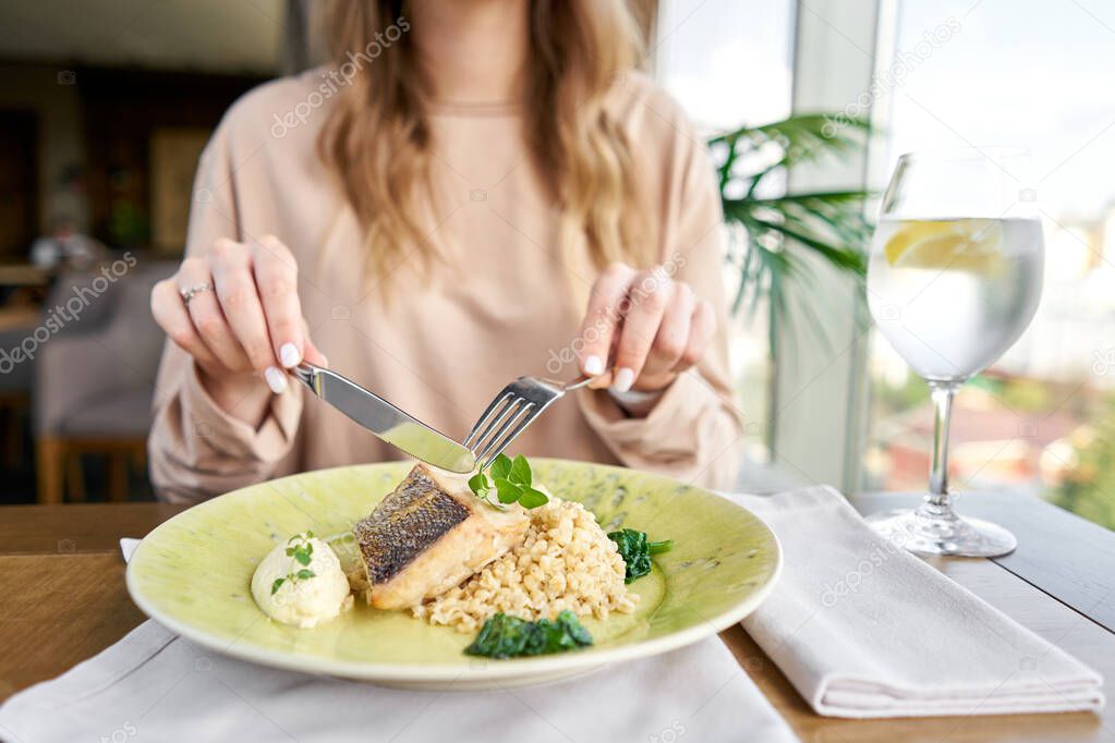 Roasted Pike perch with spelt and Polish sauce. Lunch in a restaurant, a woman eats delicious and healthy food. Dish decorated with a spinach. Restaurant menu