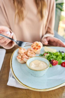 Mango-jalapeno soslu ızgara Arjantin karidesi. Bir restoranda öğle yemeği, bir kadın lezzetli ve sağlıklı yiyecekler yer. Taze sebze ve limonlu lezzetli deniz ürünleri karidesleri. Krema sosu